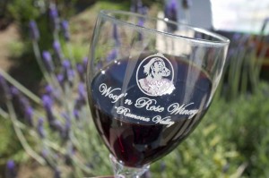 Woof'n Rose logo glass with dark red wine against a backdrop of lavender flowers.
